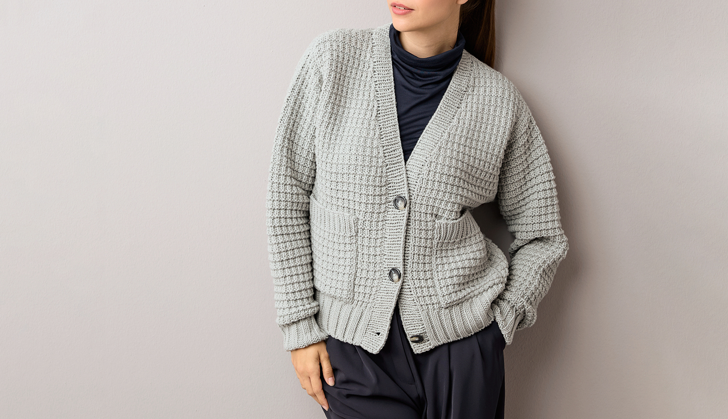 Strickanleitung Cardigan aus Classik Strickanleitung Cardigan aus Classik: Grauer Cardigan mit Knopfleiste, getragen über schwarzem Rollkragenpullover.