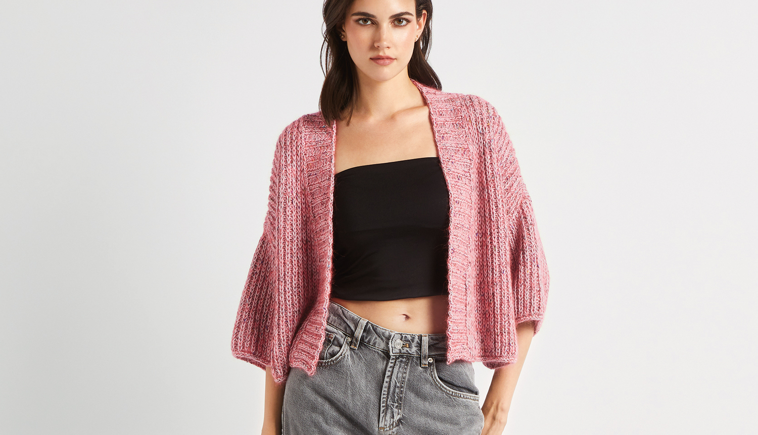 Strickanleitung Kimono-Jacke mit Beilaufgarn: Rosa Kimono-Jacke, lässig über schwarzem Top und grauer Jeans getragen.