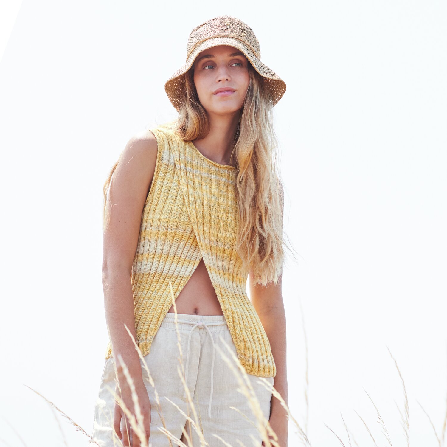 Strickset Top Modell 07 aus Lovewool No. 22: Frau in gelbem Stricktop und Strohhut in sommerlicher Landschaft.
