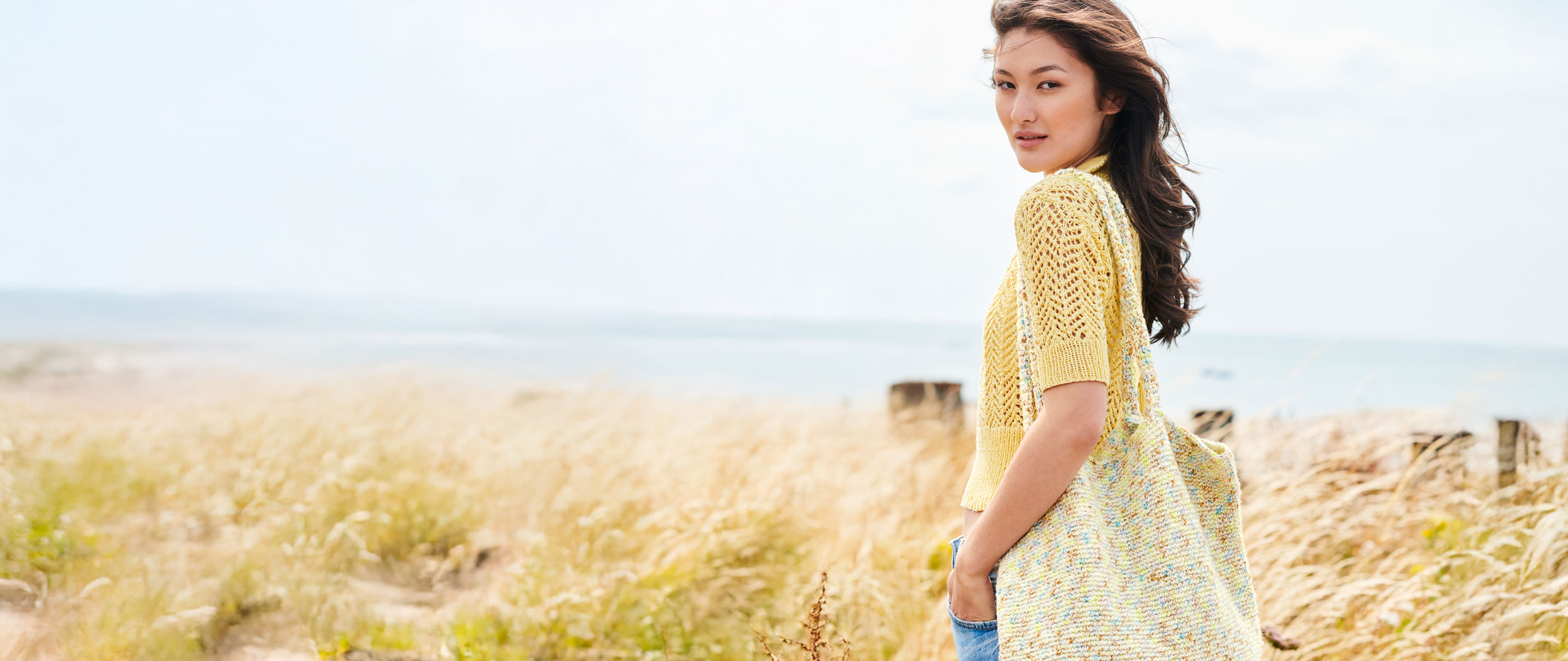 Frau mit gelbem Strickshirt steht vor Düne
