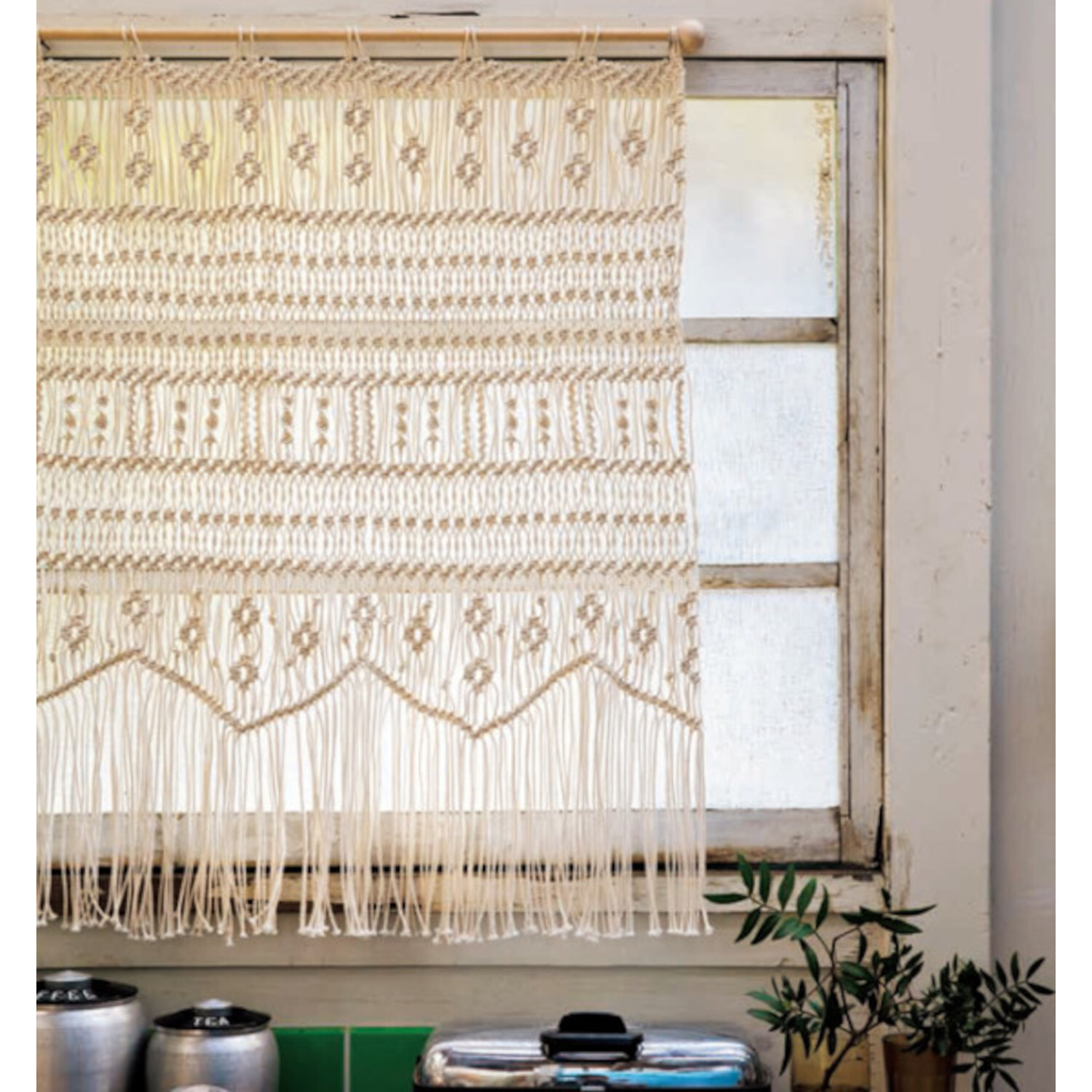 New Makramee - 25 Knüpfprojekte: Elegantes Makramee-Wandbehang in Creme vor einem Fenster.