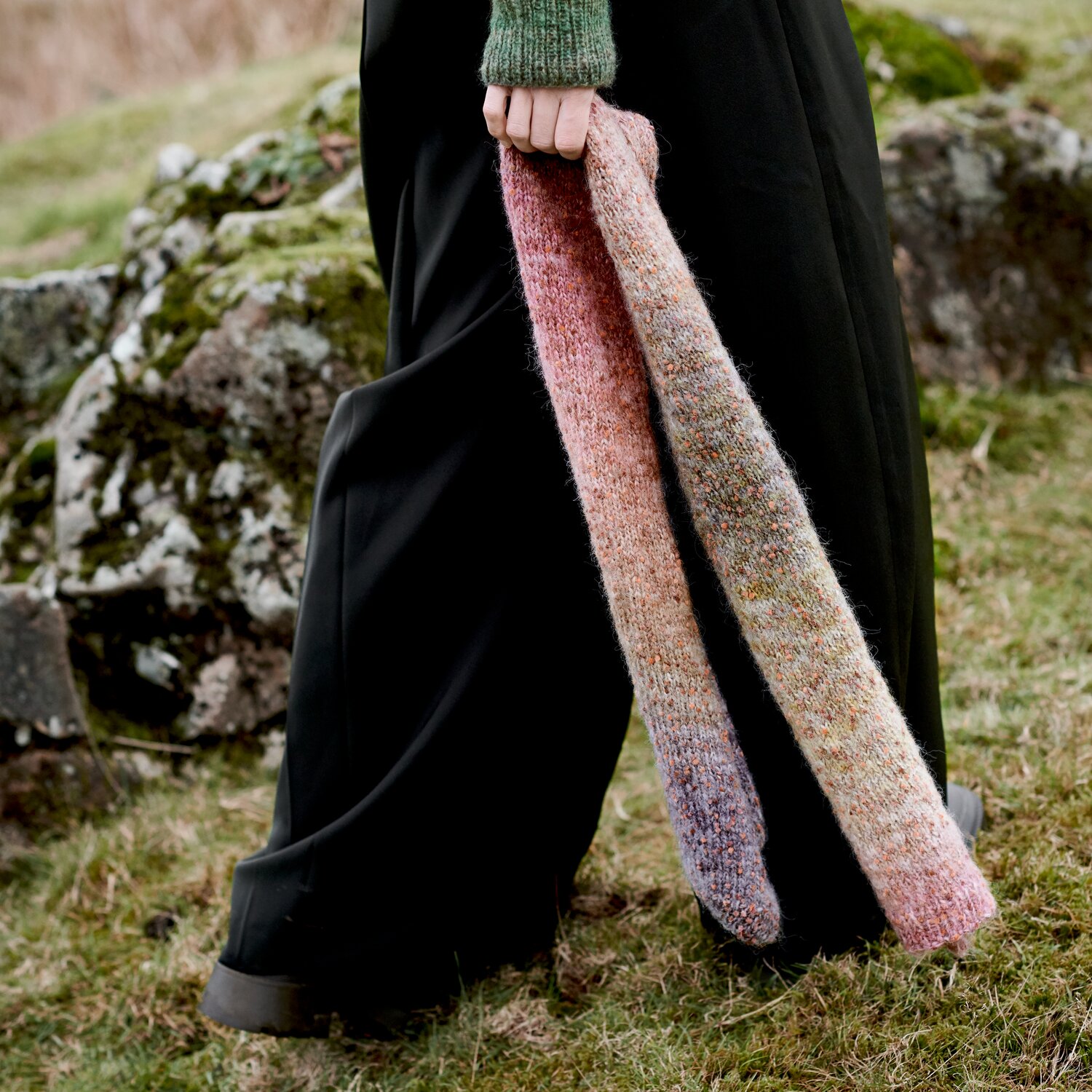 Strickset Schal Modell 25 aus Lovewool No. 23, langer melierter Schal in Naturtönen, getragen im Freien zu schwarzer Hose und grünem Strickpullover