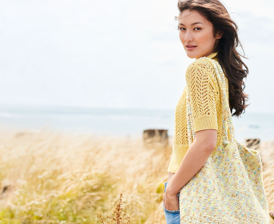 Frau mit gelbem Strickshirt steht vor Düne