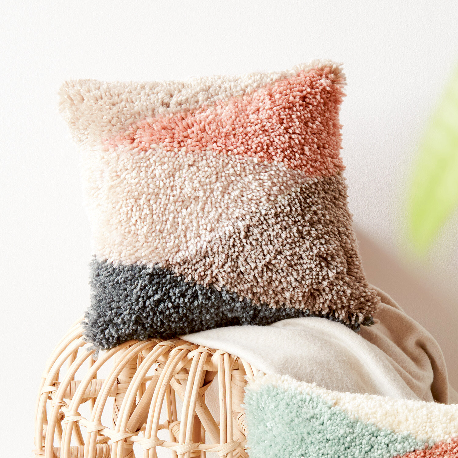 Anleitung Knüpfen Kissen mit Dreiecksmuster: Flauschiges Kissen in Beige, Rosa und Grau auf Korbstuhl.