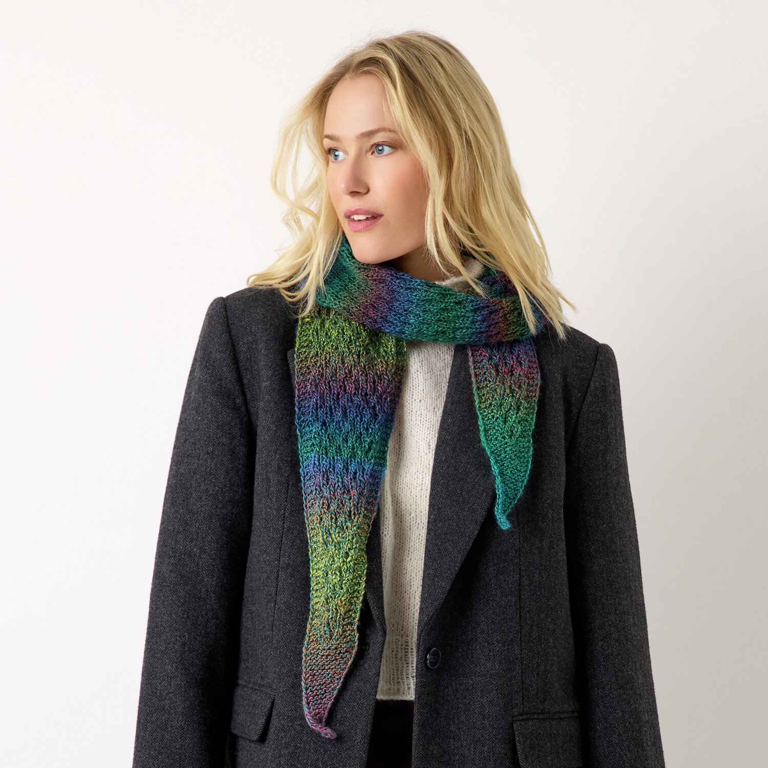 Strickset Dreieckstuch Modell 28 aus Die Neue Masche No. 13 von idee. Creativmarkt Strickset Dreieckstuch Modell 28: Frau trägt farbenfrohes Tuch über grauem Mantel, ideal für kühle Tage.