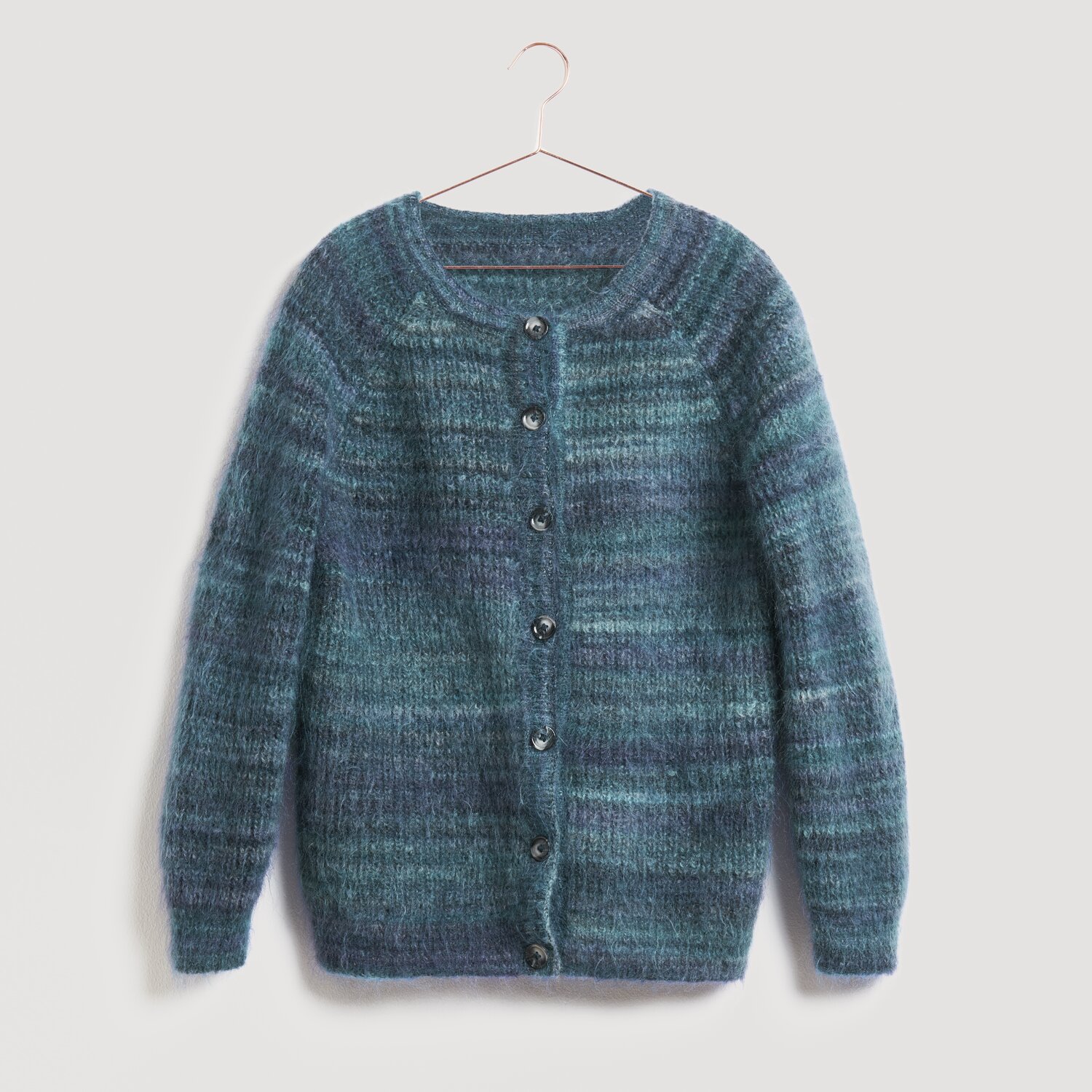 Strickjacke in Blau- und Grüntönen, aufgehängt an einem Haken. Die Jacke ist von der Marke Modell Legeware und hat einen klassischen Rundhalsausschnitt mit Knopfleiste. Ideal für kühle Tage.