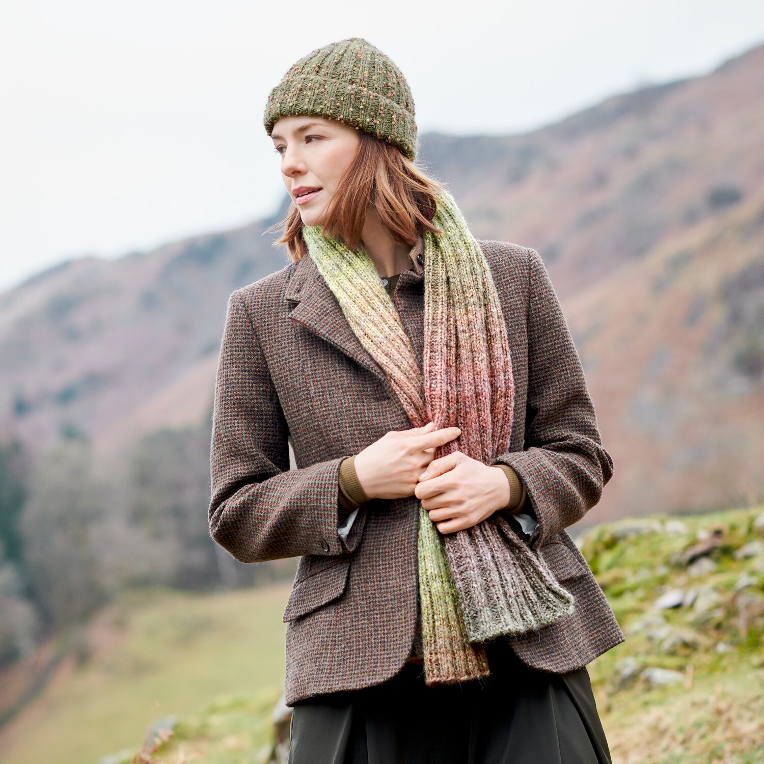 Strickset Schal Modell 23 aus Lovewool No. 23 mit passender Strukturmütze Modell 16a, getragen von Frau im Outdoor-Look vor herbstlicher Berglandschaft