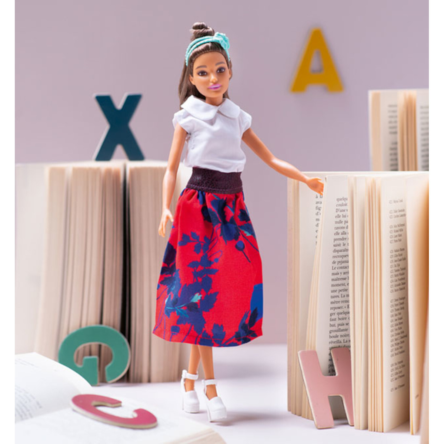 Barbie - Kleidung für Barbie und Ken selbst nähen: Puppe in weißem Oberteil, rotem Rock, umgeben von Büchern und Buchstaben.