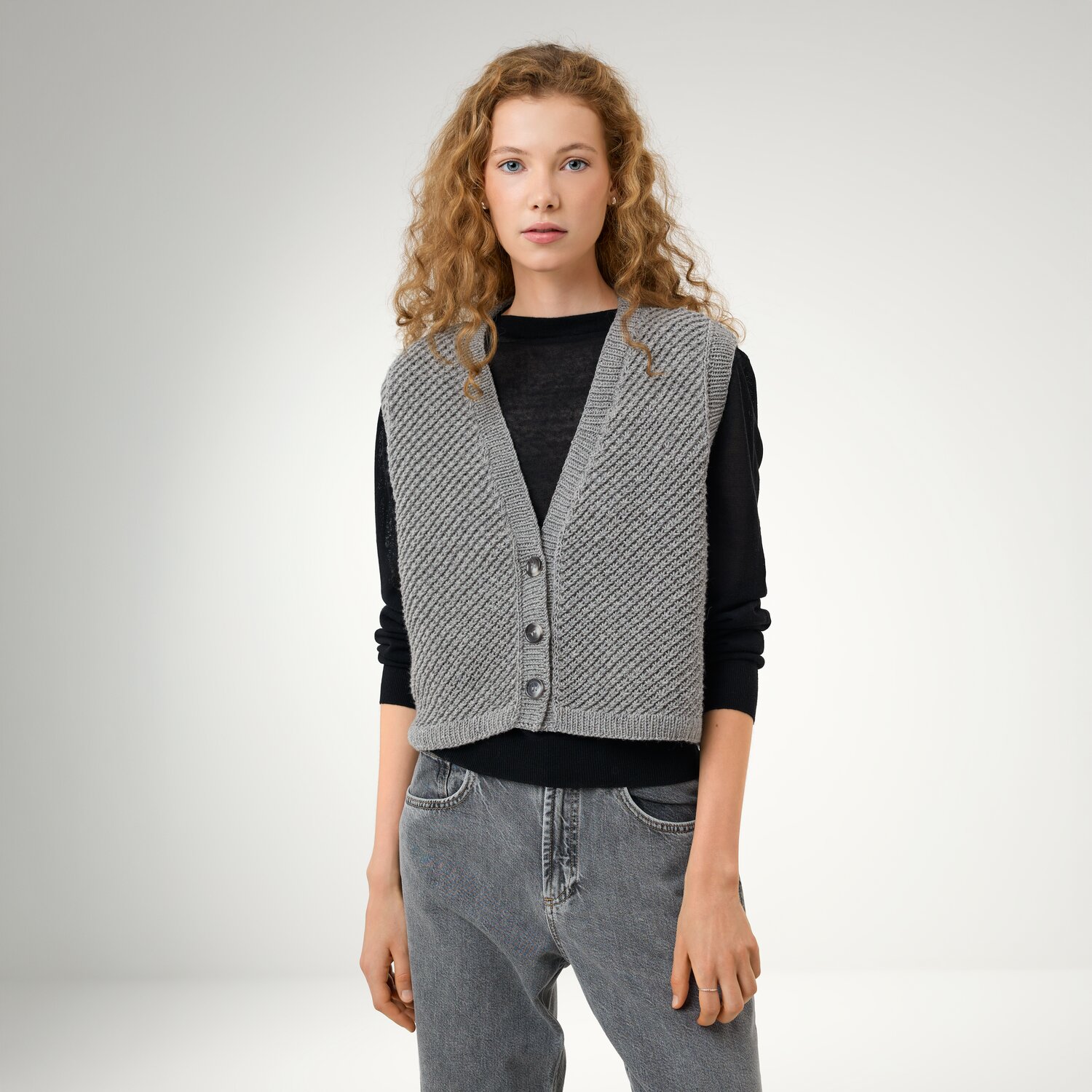 Strickset Weste Modell 2a aus Die Neue Masche No. 16, ärmellose Strickweste mit Knopfleiste über schwarzem Langarmshirt, kombiniert mit Jeans im Studio.