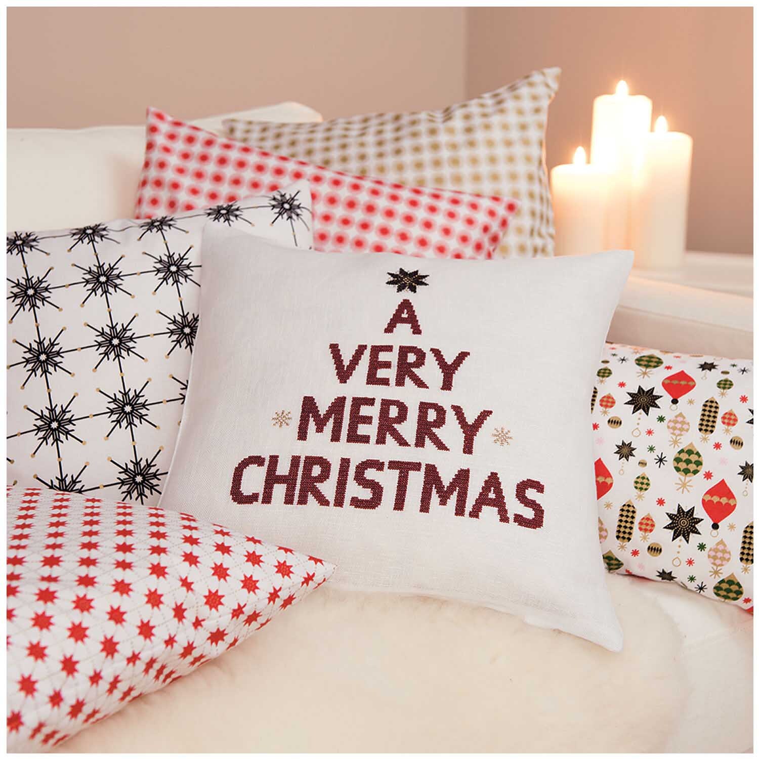 Stoff Rosette rot 50x140cm von Rico Design Stoff Rosette rot 50x140cm von Rico Design: Weihnachtskissen auf Sofa mit Kerzen im Hintergrund.
