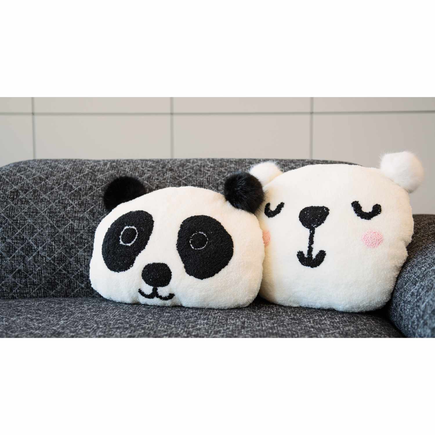 Meterware Teddyplüsch: Zwei weiche Kissen in Panda- und Bärform auf einem grauen Sofa. Ideal für gemütliche Wohnräume.