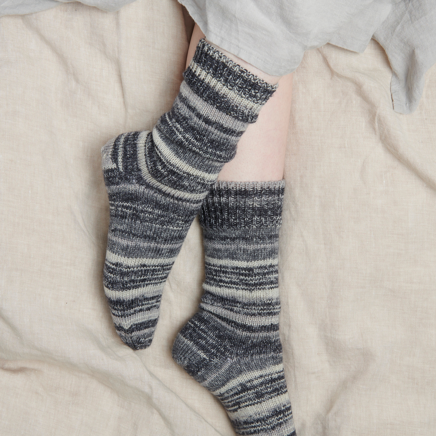 Socks Earth + Wind + Fire 6-fädig von Rico Design in Grautönen, getragen an Füßen auf beigem Stoff.