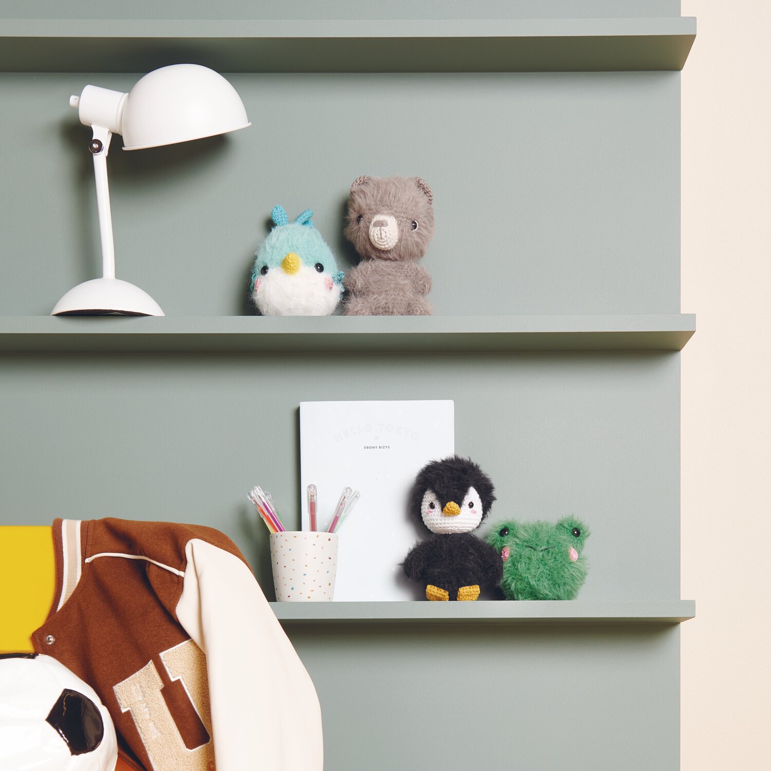 Creative Ricorumi dk 25g Farbe Senf von Rico Design Ricorumi Furry Animals auf grünem Regal mit Lampe und Schreibutensilien, dekoriert mit Plüschtieren.