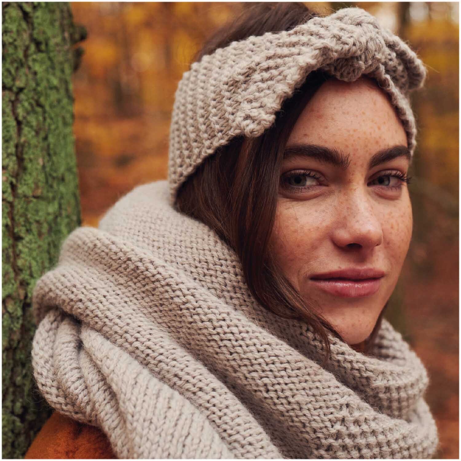 Essentials Alpaca Twist Chunky: Frau trägt gestricktes Stirnband und Schal in herbstlicher Waldkulisse.