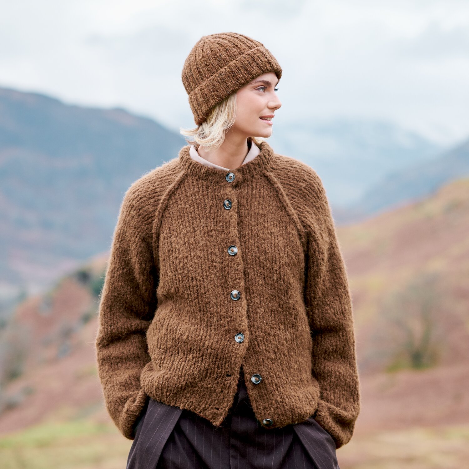 Strickset Jacke Modell 34 aus Lovewool No. 23, locker geschnittene, grobgestrickte Knopfjacke mit passender Mütze, getragen von Frau vor herbstlicher Berglandschaft