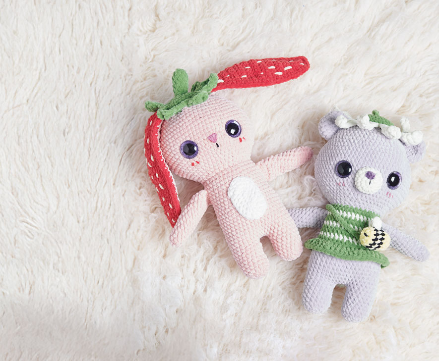 Gehäkelter Hase und gehäkelter Dinosaurier liegen auf hellem Teppich