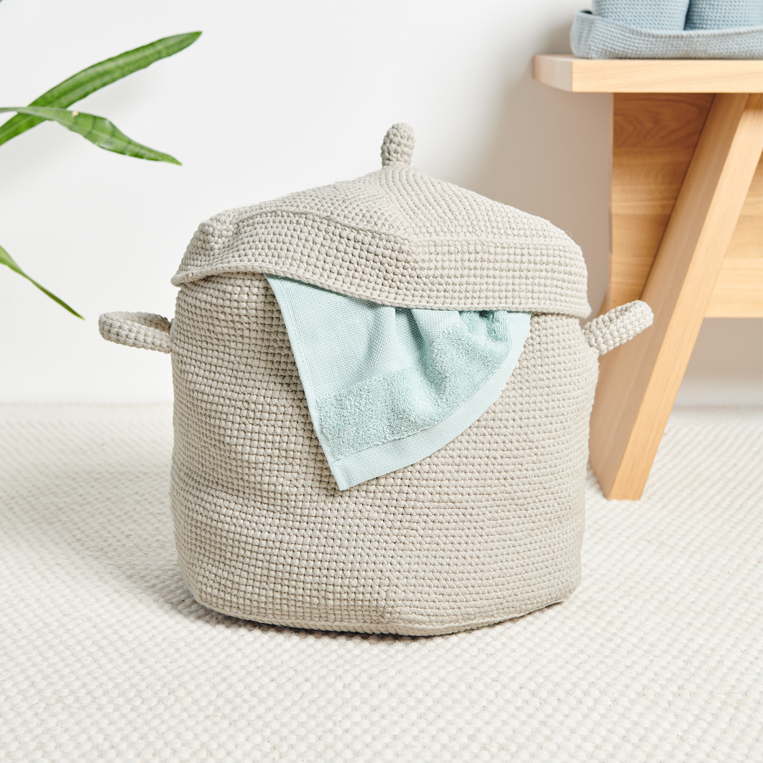 Häkelanleitung Korb aus Fashion Jersey: Beiger, gehäkelter Korb mit Deckel und seitlichen Griffen auf hellem Teppich.