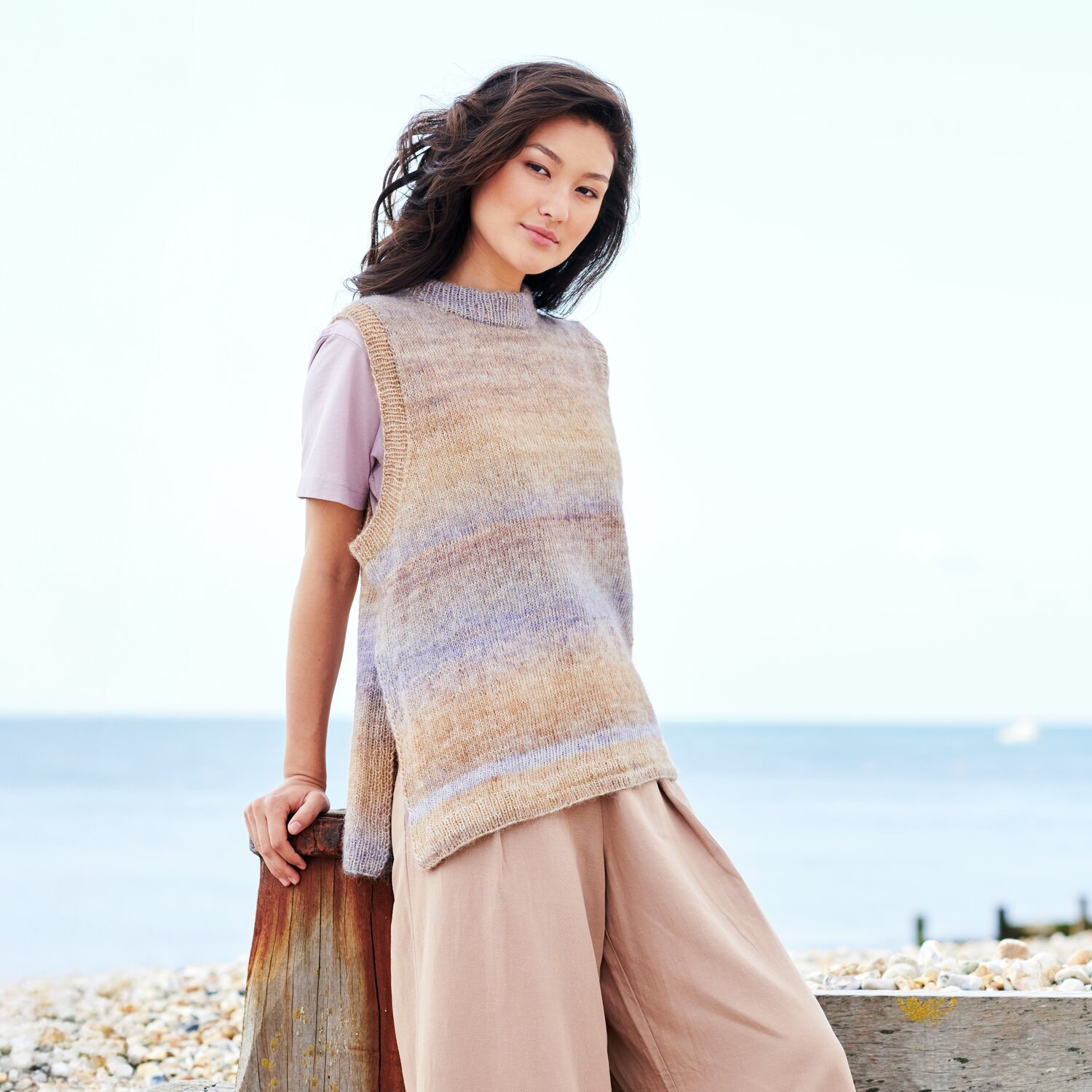 Strickset Pullunder Modell 15 aus Lovewool No. 22: Frau am Strand in pastellfarbenem Pullunder vor blauem Meer.