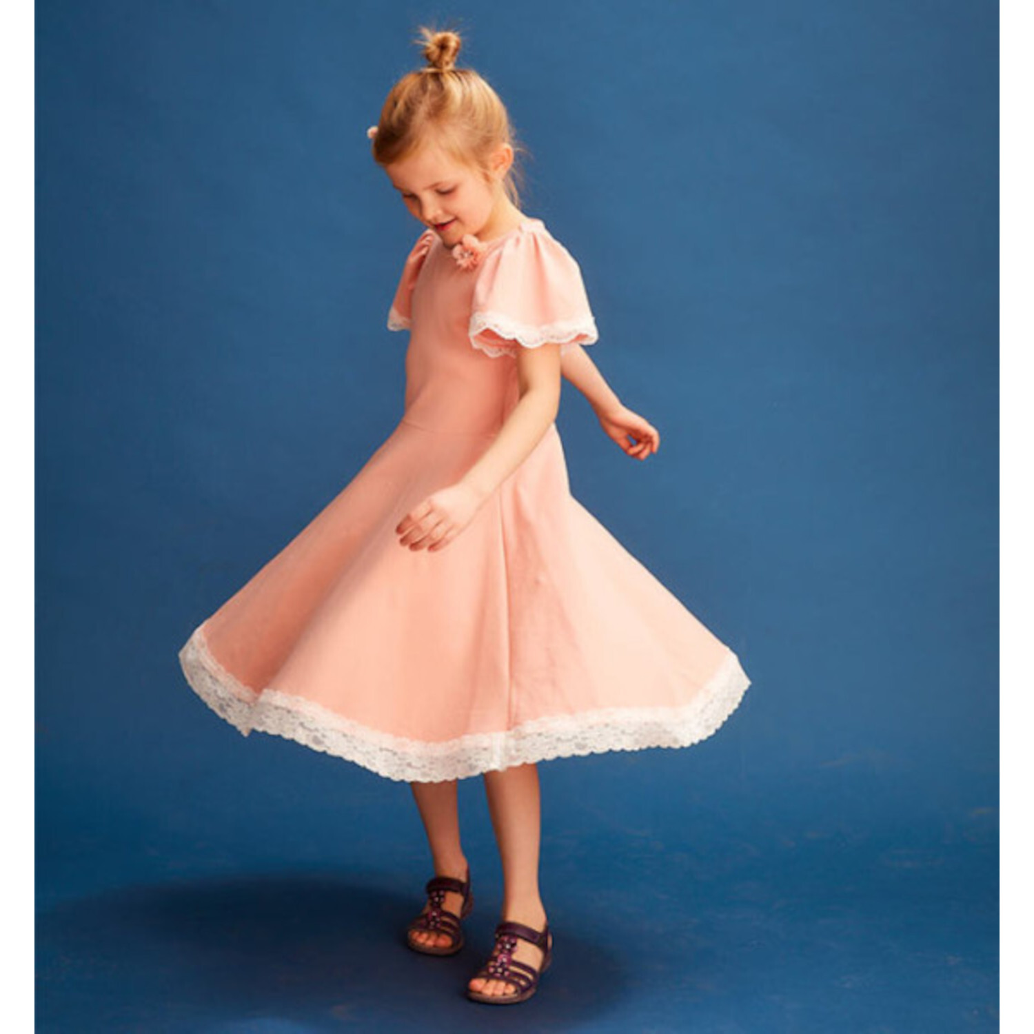 Der Jersey Kleiderbaukasten für Kids: Mädchen in rosa Kleid mit Spitzenrand, dreht sich vor blauem Hintergrund.