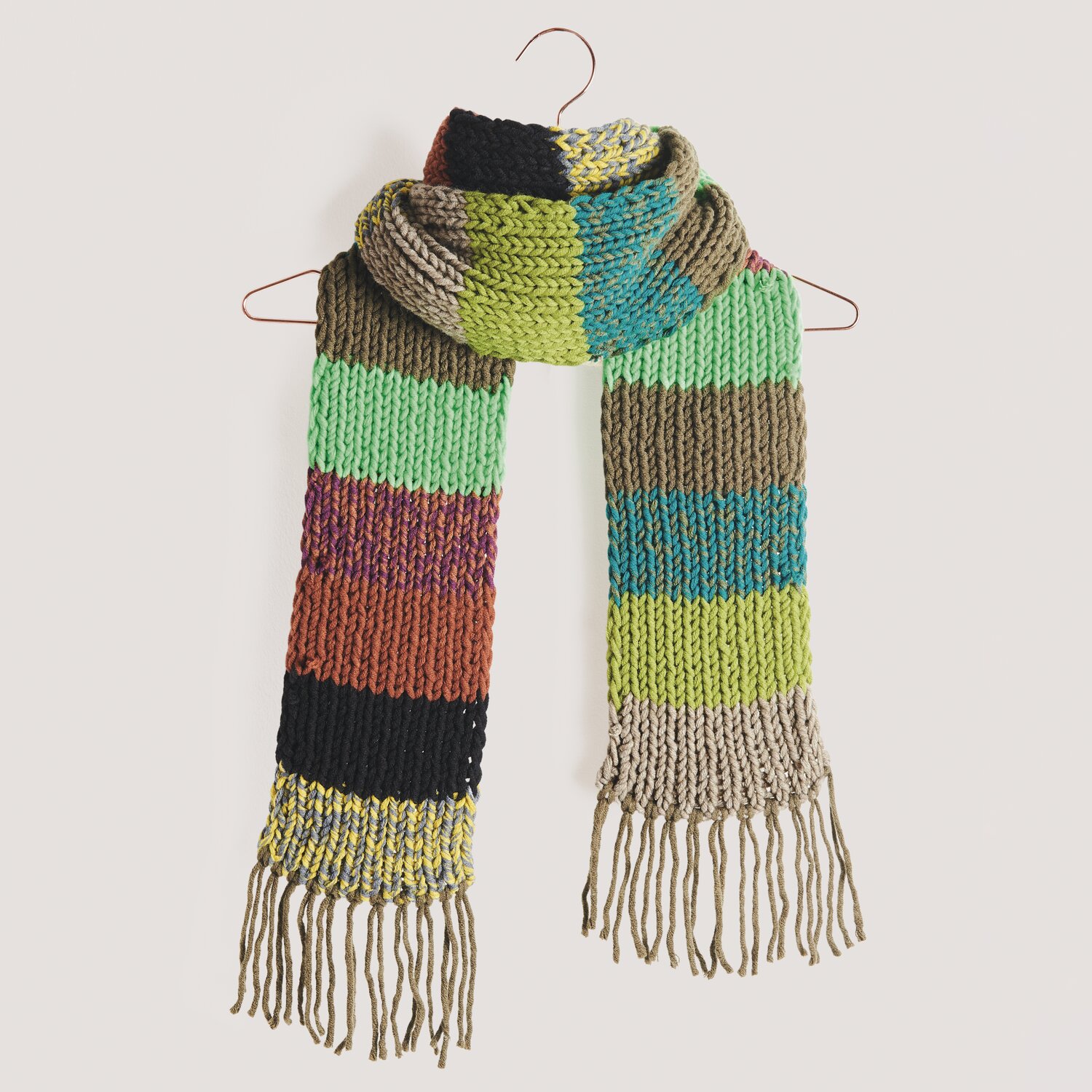 Garnset „Schal des Jahres“: Bunter, gestrickter Schal mit Fransen, präsentiert auf einem Kleiderbügel.