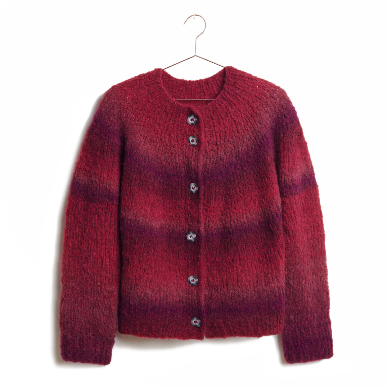 Eine Jacke aus einem rot-beerigen Farbverlaufsgarn gestrickt hängt an einem Kleiderbügel.