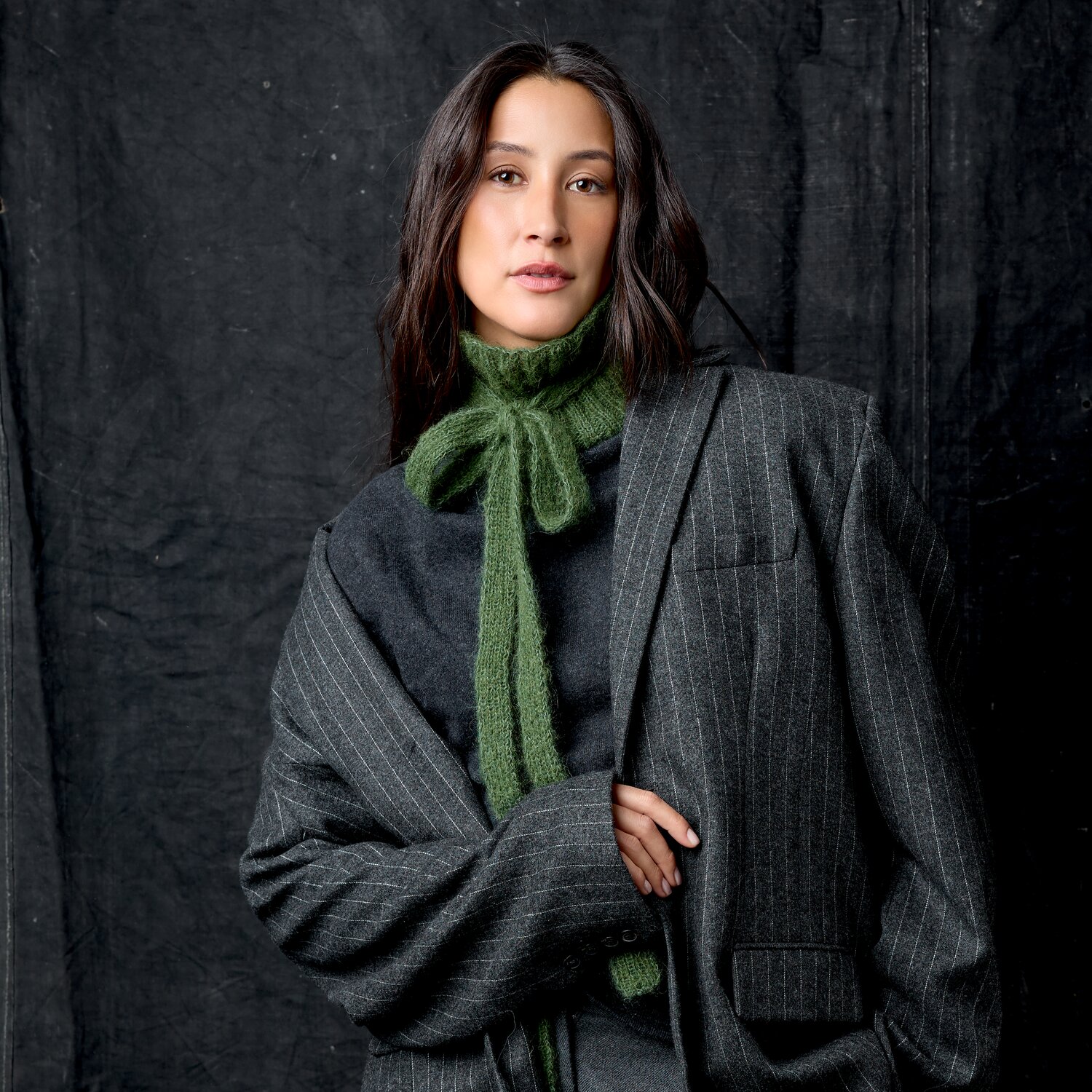 Strickset Kragen Modell 07 aus Luxury Knits Little Pieces, gestrickter grüner Schlaufenkragen an Frau mit dunkelgrauem Nadelstreifenblazer vor dunklem Hintergrund