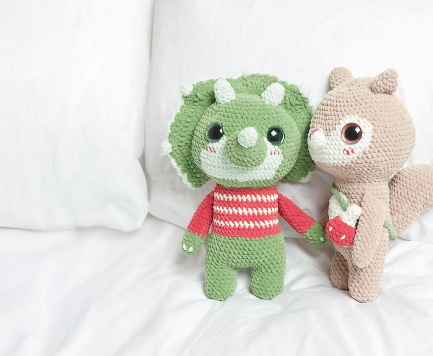 Gehäkelter Dinosaurier und gehäkeltes Eichhörnchen sitzen auf einem Bett