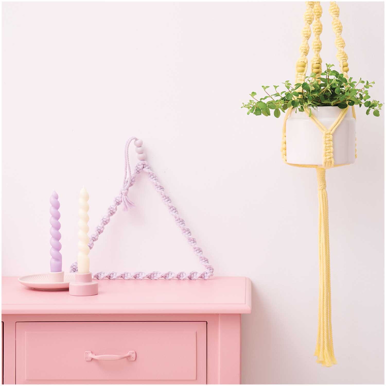 Creative Cotton Cord Makramee-Garn: Lavendelfarbene Dekoration mit Pflanzenhänger und Kerzen auf rosa Kommode. Ideal für kreative Wohnideen.