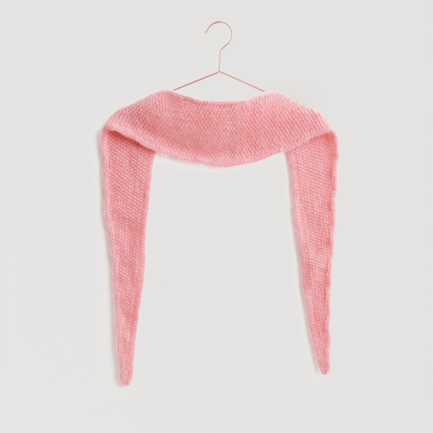Ein weiches, rosa Strickschal von Modell Legeware hängt auf einem Kleiderbügel. Der Schal hat eine gleichmäßige Textur und ist ideal für kühle Tage. Perfekt für modische Akzente.