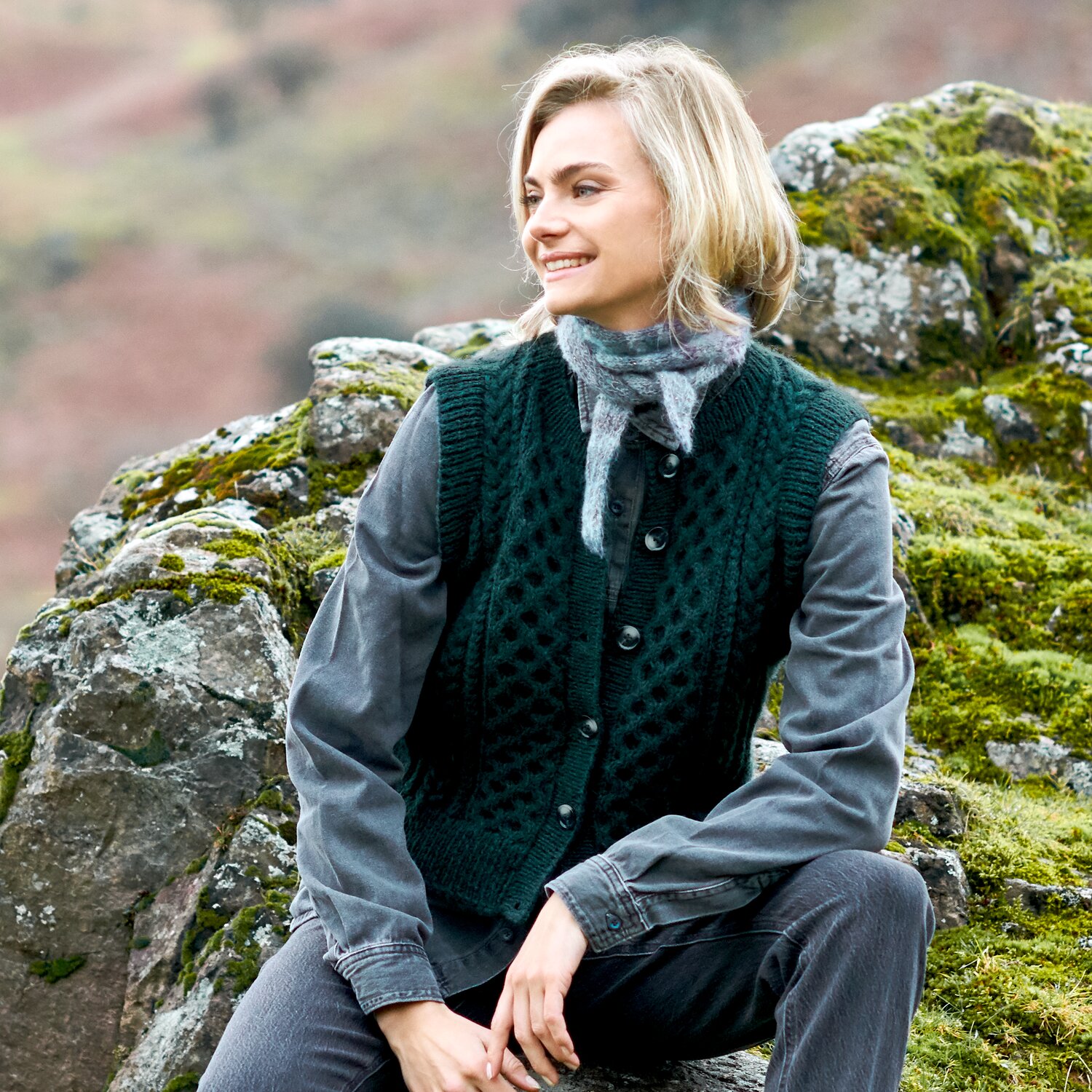 Strickset Weste Modell 13 aus Lovewool No. 23, gehäkelte Herrenweste in dunklem Grün, kombiniert mit grauem Hemd und Schal, getragen in felsiger Naturkulisse