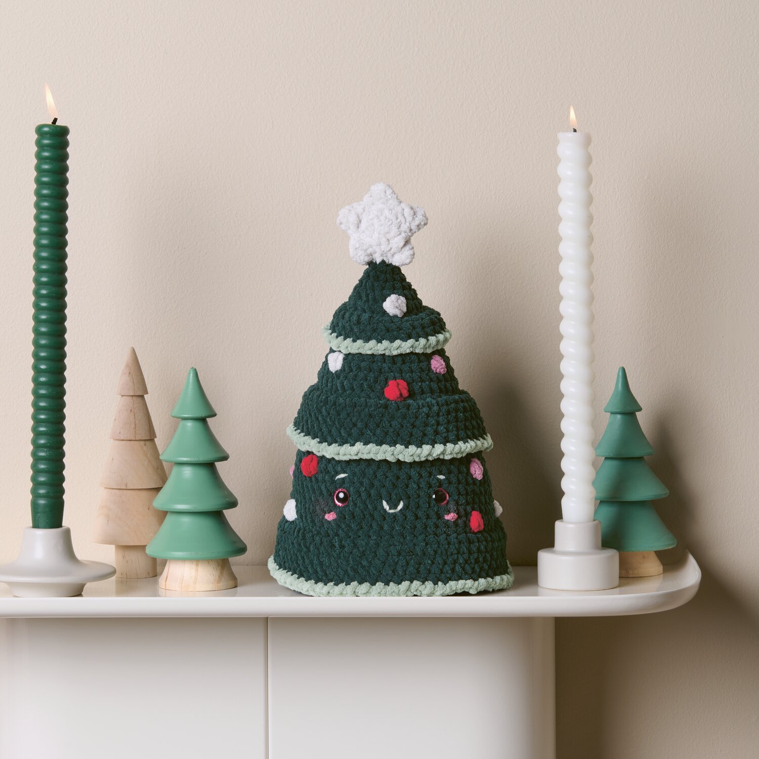 Creative Chenillove Sparkle 100g 110m Farbe Beere von Rico Design Häkelset Weihnachtsbaum Modell 4 aus Chenillove Sparkle Christmas: Grüner Baum mit Dekoration auf weißem Tisch, umgeben von Kerzen und kleinen Bäumen.