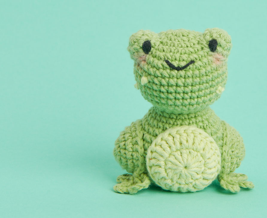 Gehäkelter Frosch sitzt vor grünem Hintergrund