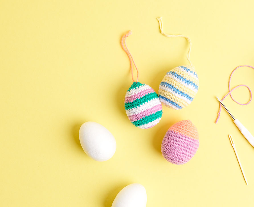 Gehäkelte Ostereier liegen auf gelbem Untergrund