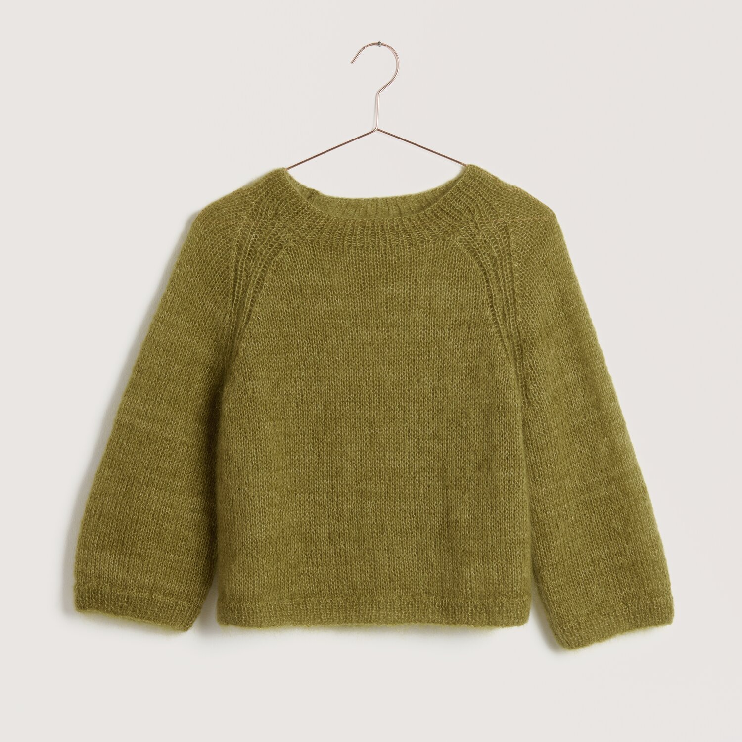 Strickset Pullover Modell 18 aus Lovewool No. 22 in Weide. Handgestrickter Pullover auf einem Kleiderbügel vor neutralem Hintergrund.