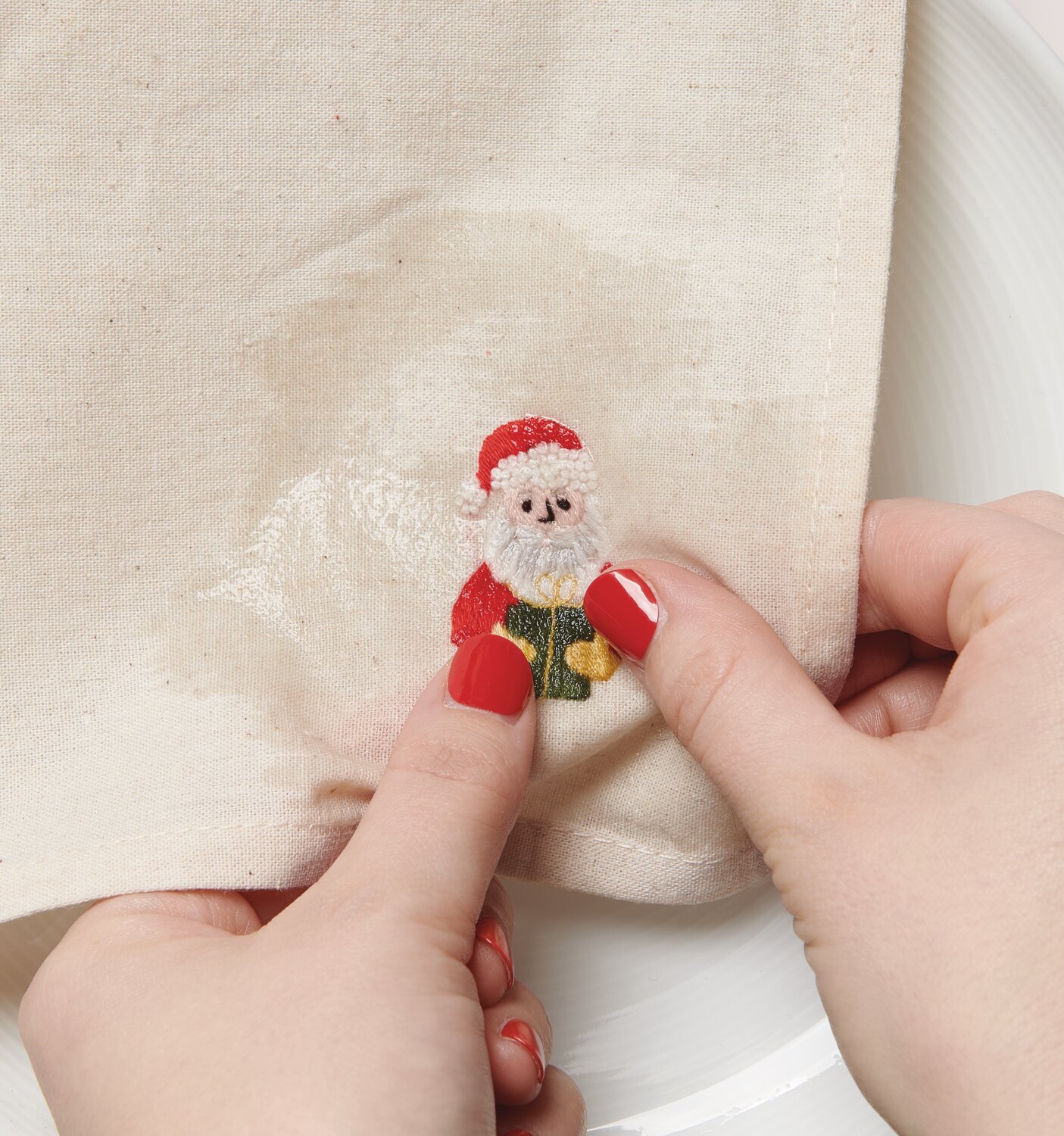 Stick & Stitch Stickpackung Weihnachtsmann 13 Stück: Hände halten ein besticktes Tuch mit Weihnachtsmann-Motiv.