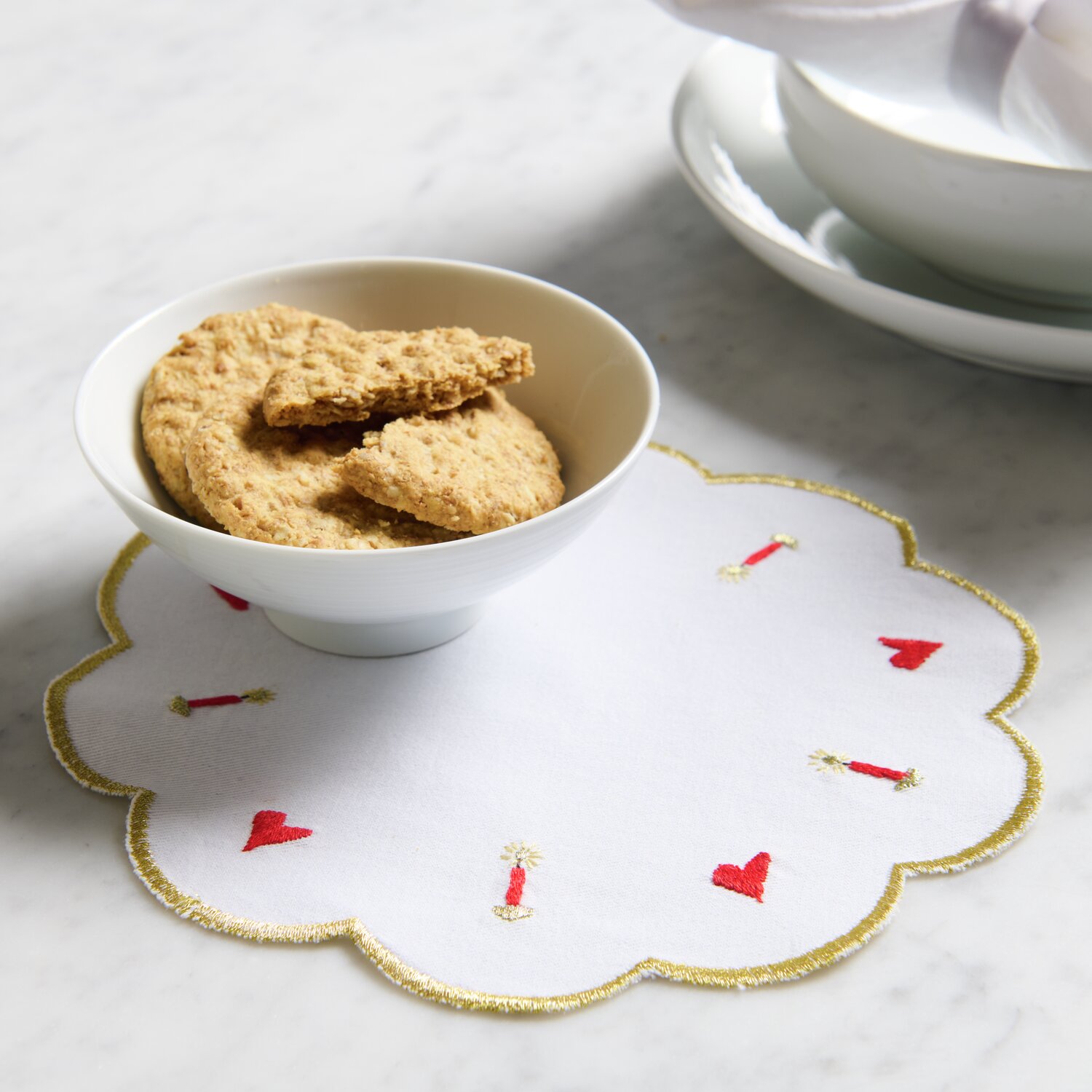 Stick & Stitch Stickpackung Engel mit Kerzen 16 Stück: Weißes Deckchen mit roten Herzen und Kerzenstickerei, präsentiert mit Keksen in einer Schale.