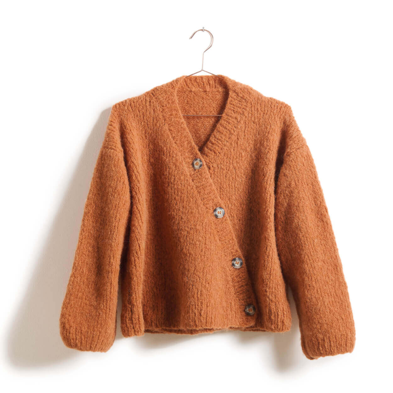 Orangefarbene Strickjacke mit V-Ausschnitt, Knopfleiste und flauschiger Struktur auf Kleiderbügel vor hellem Hintergrund