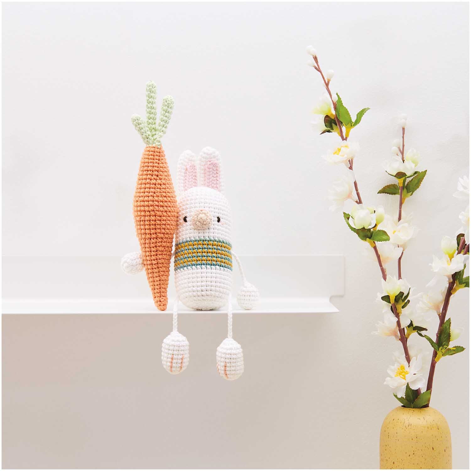 Creative Ricorumi dk: Häkelfigur Hase mit großer Karotte, dekorativ auf einem Regal platziert.