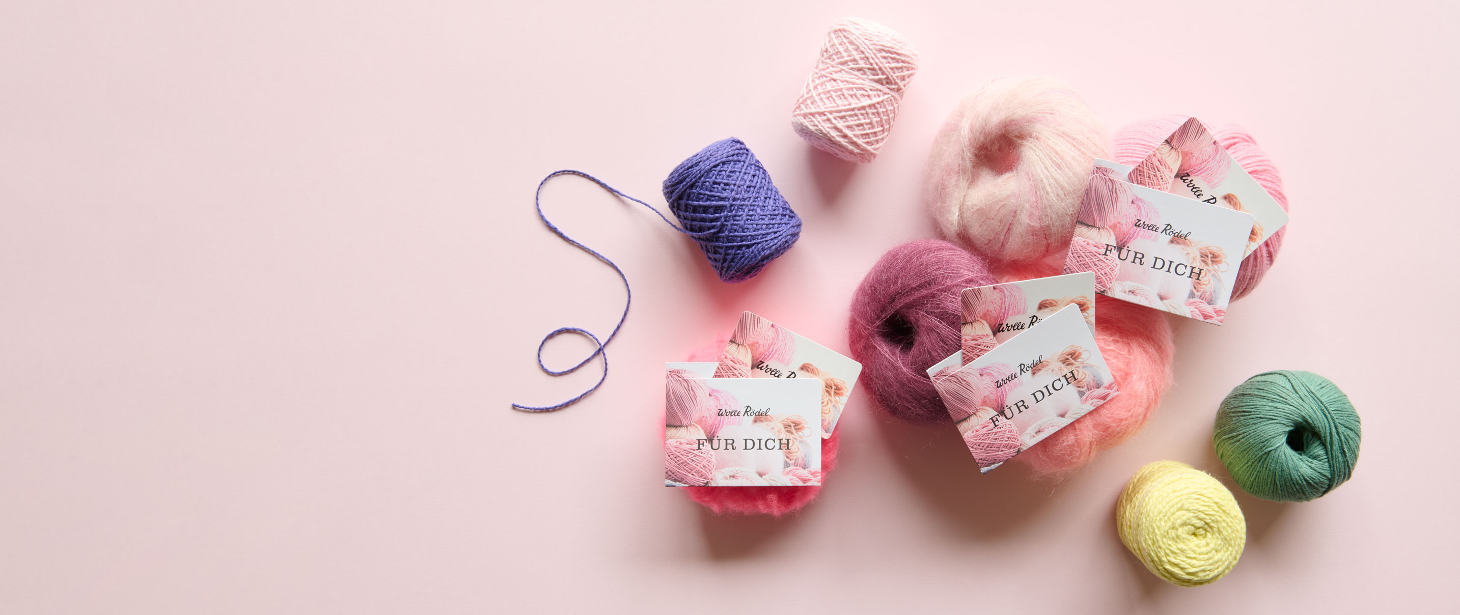 3 Wolle Rödel Geschenk-Karten liegen auf bunten Wollknäuel