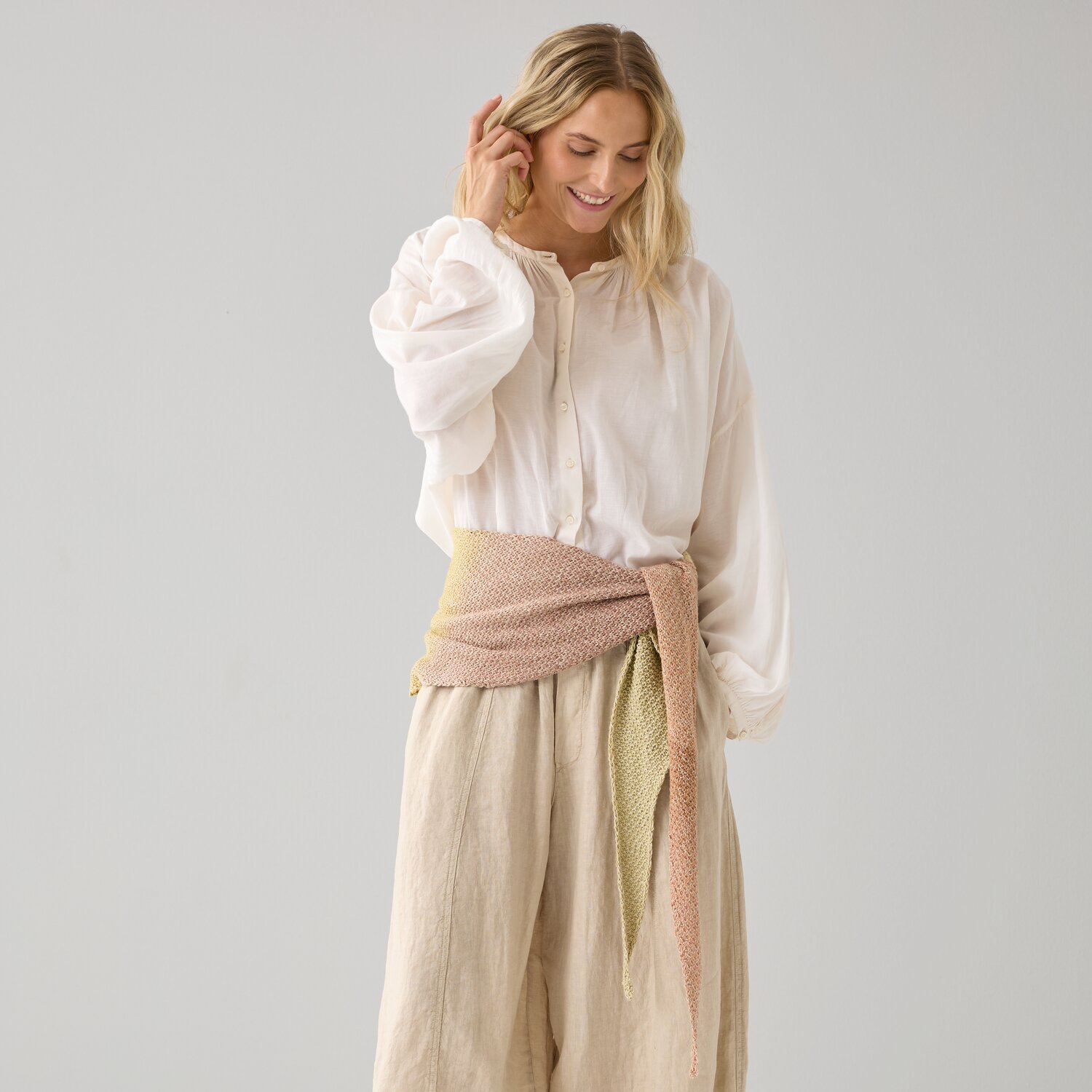 Strickset Dreieckstuch Modell 16: Frau trägt ein pastellfarbenes Tuch um die Taille, kombiniert mit heller Kleidung.