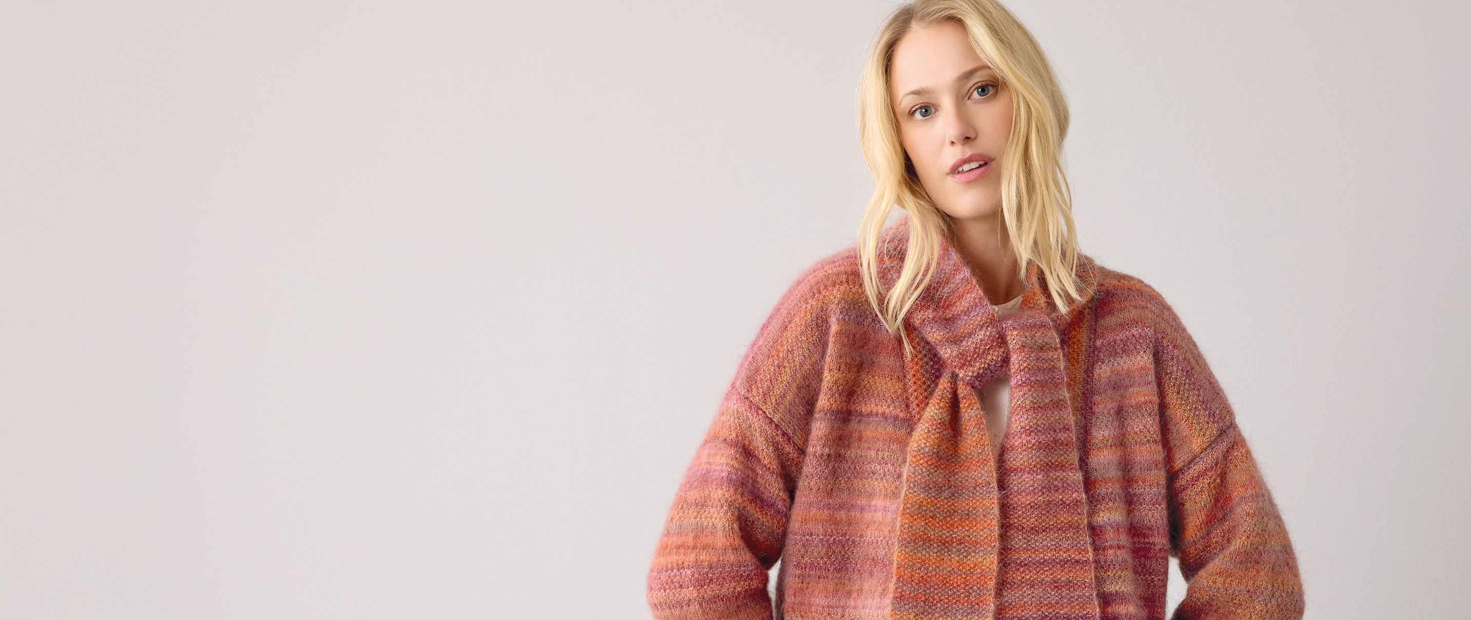 Frau trägt orange gestreiften Strickschal und Strickjacke vor hellem Hintergrund