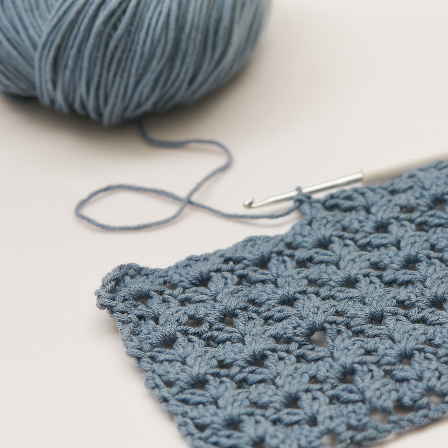 Creative Sport dk Die Neue Masche No. 9 Frühjahr-Sommer, gehäkelte Probe mit Strukturmuster in taubenblauer Wolle, daneben Knäuel und Häkelnadel von Rico Design
