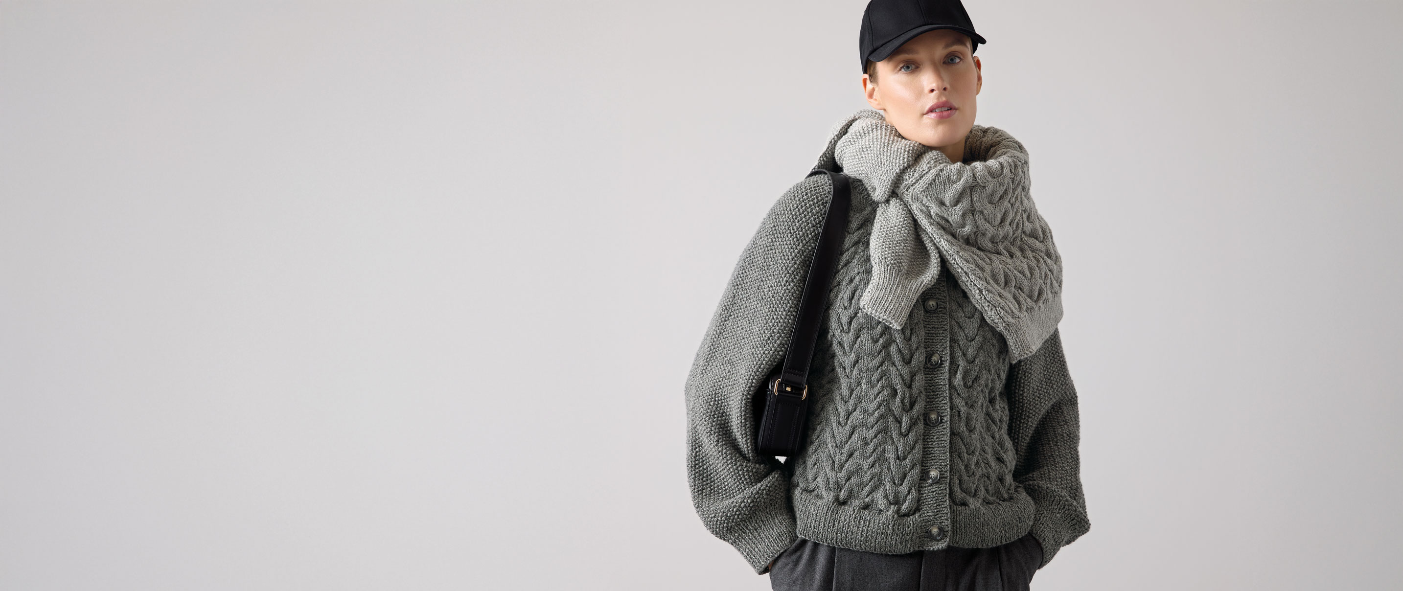 Frau trägt dunkelgrauen Strickpulli und hellgrauenStrickpulli um die Schultern gebunden.