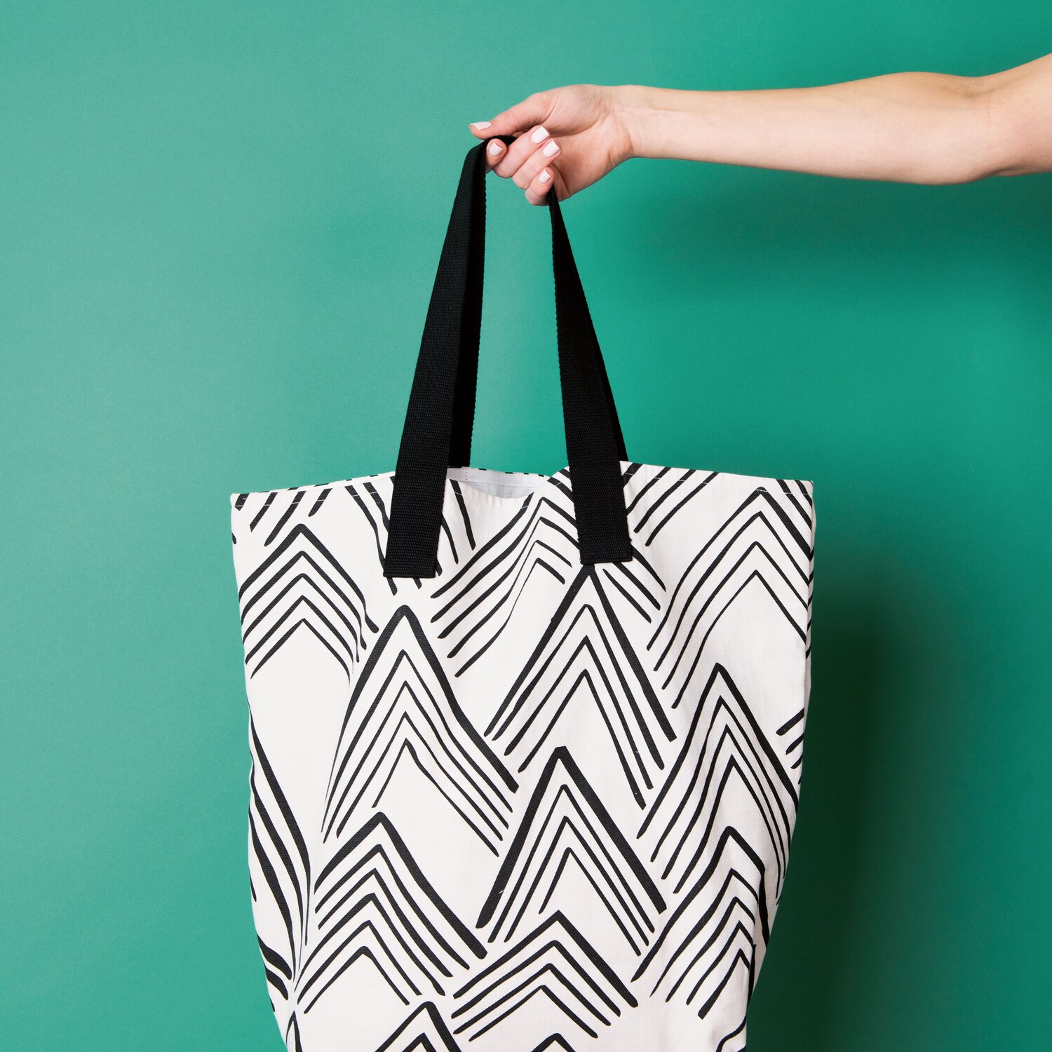 Gurtband 40mm 2m von Rico Design an großer Stofftasche mit grafischem Muster, stabile Tragegriffe werden von Hand vor türkisfarbenem Hintergrund präsentiert.