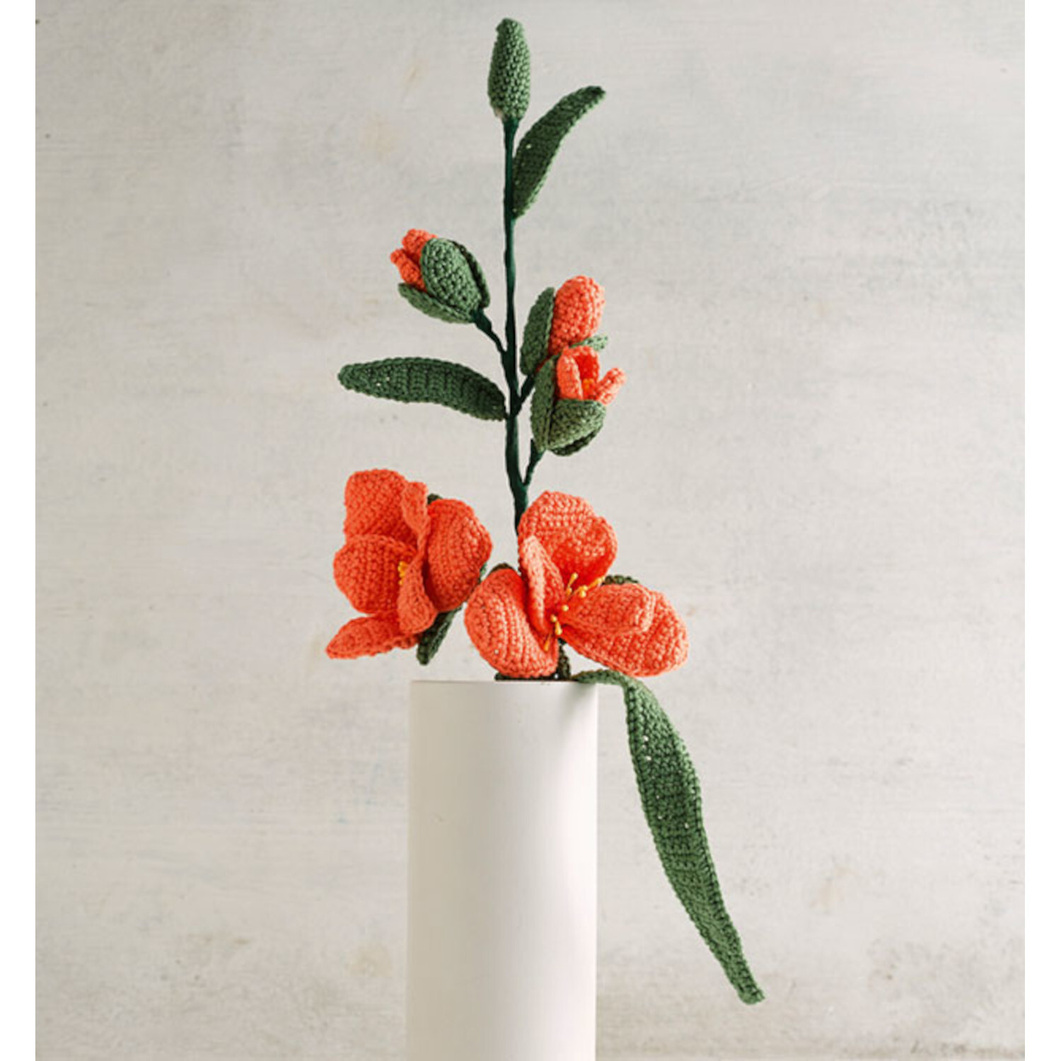 Häkeln so bunt wie die Natur: Handgefertigte orange Blumen in weißer Vase, dekorativ und stilvoll.
