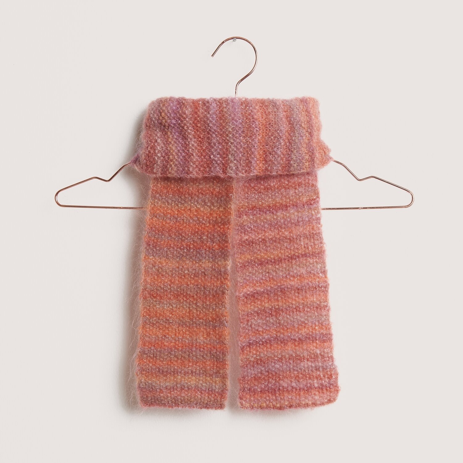 Fashion Meri Mohair Print 50g 275m Farbe Happy Sunrise von Rico Design Fashion Meri Mohair Print Schal in Rosa-Orange auf einem Kleiderbügel, ideal für kühle Tage.