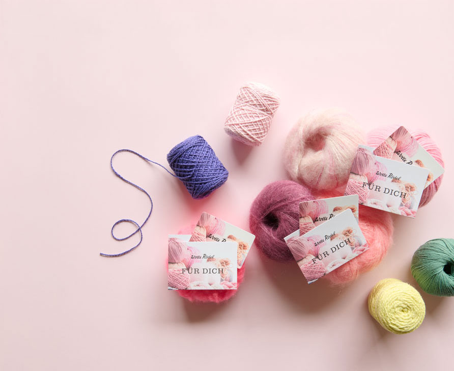 3 Wolle Rödel Geschenk-Karten liegen auf bunten Wollknäuel