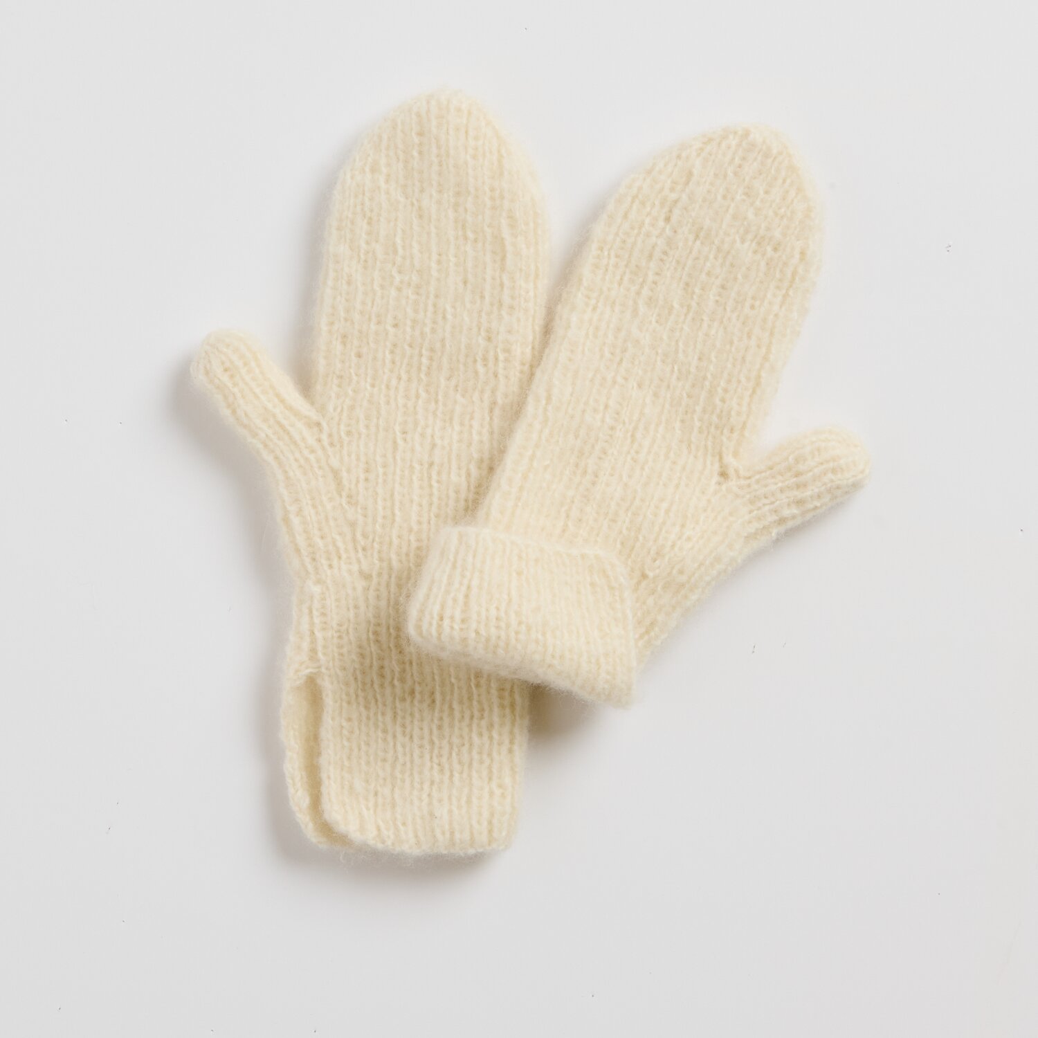 Strickset Fäustlinge Modell 12 aus Luxury Knits Little Pieces, weiche cremefarbene Wollfäustlinge mit umgeschlagenem Bündchen, liegend auf hellem Untergrund