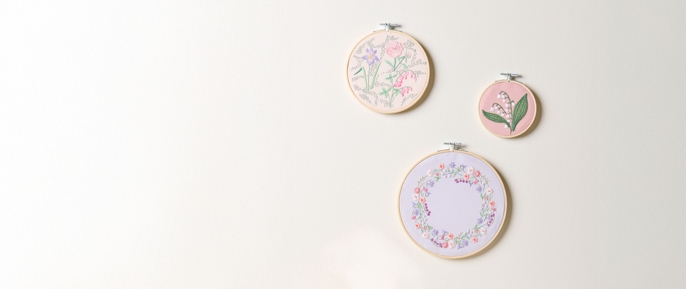 3 Stickringe mit Blumenstickbildern hängen an einer Wand