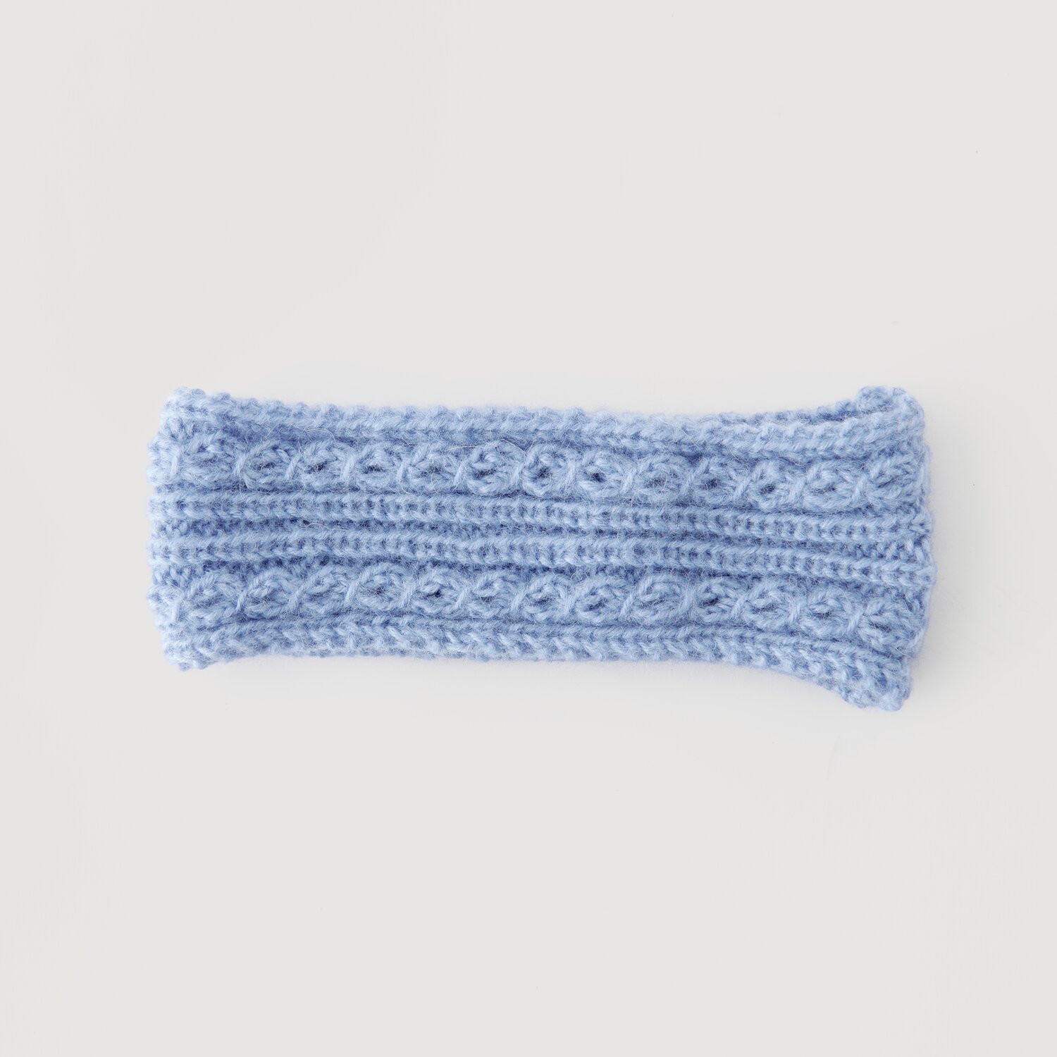 Stirnband aus hellblauer Wolle mit Zopfmuster, Modell Legeware. Ideal für kalte Tage, bietet es stilvollen Schutz. Perfekt für Modebewusste, die Komfort schätzen.